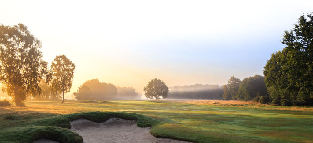 Sunrise mist over the heathland at Fulford Golf Club, with a bunker in the foreground and a flag in the distance