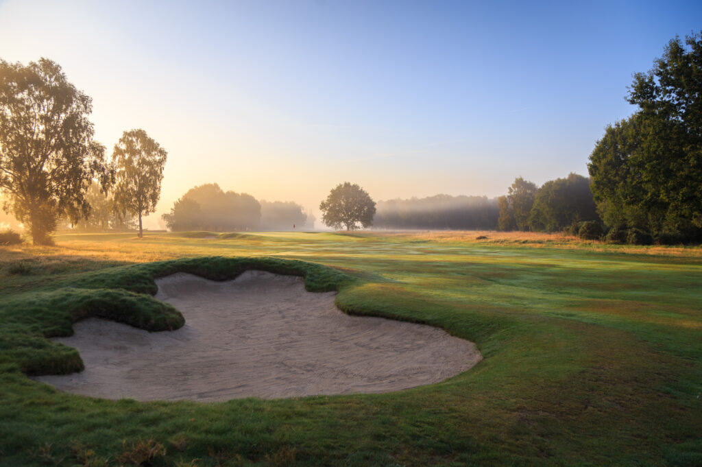 A sculpted bunker in the foreground of a misty sunrise fairway at Fulford Golf Club, York