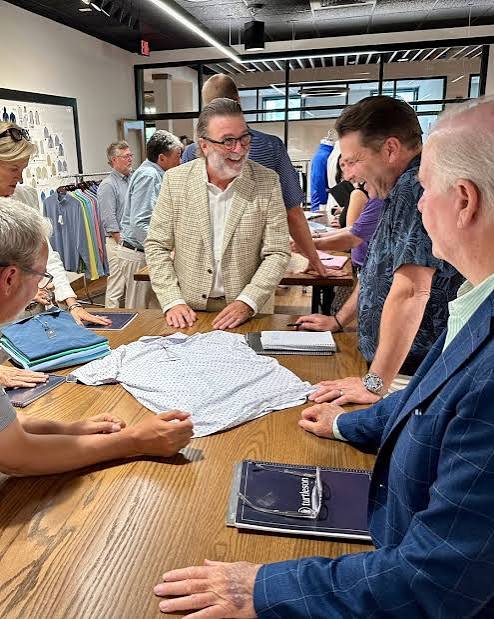 A group gathered around a wooden table looking over Turtleson shirts and samples